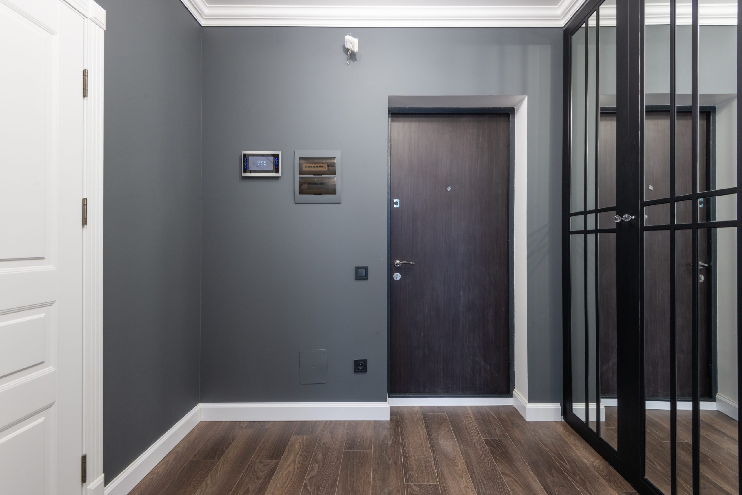 Dark wood door at the end of a hallway with a smart home control touchpad to the left.
