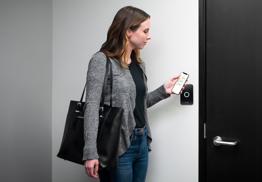 Woman holding smart phone to security panel by door.