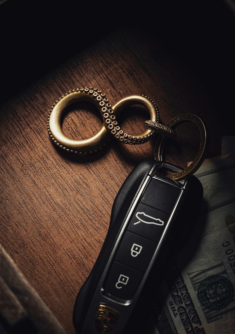 Luxury car key fob with a gold infinity-shaped keychain resting on a wooden surface beside dollar bills.