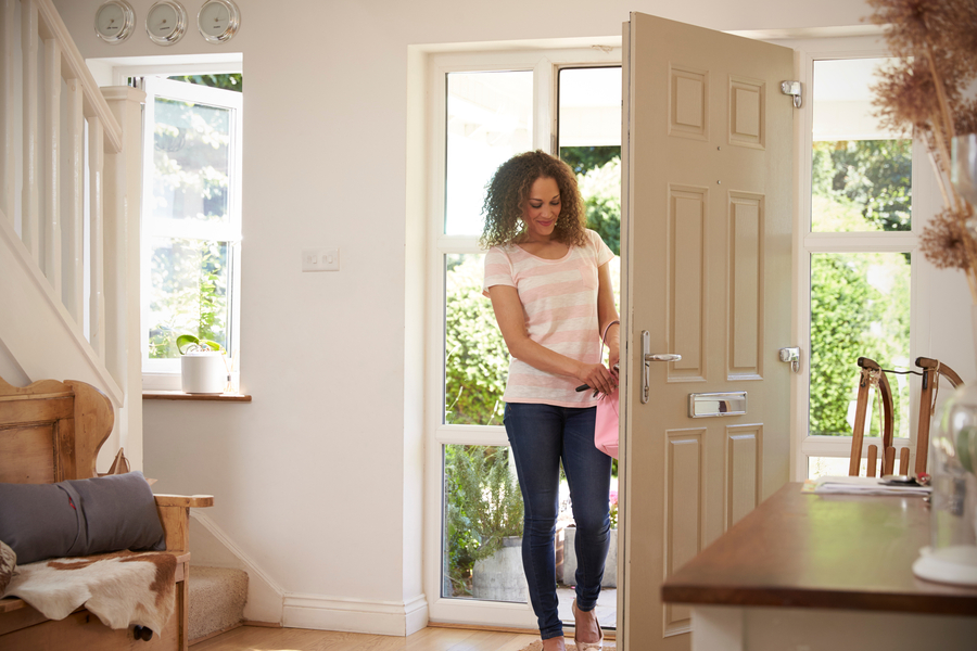 Young woman in jeans and a striped shirt opening her front door to enter her home’s foyer.